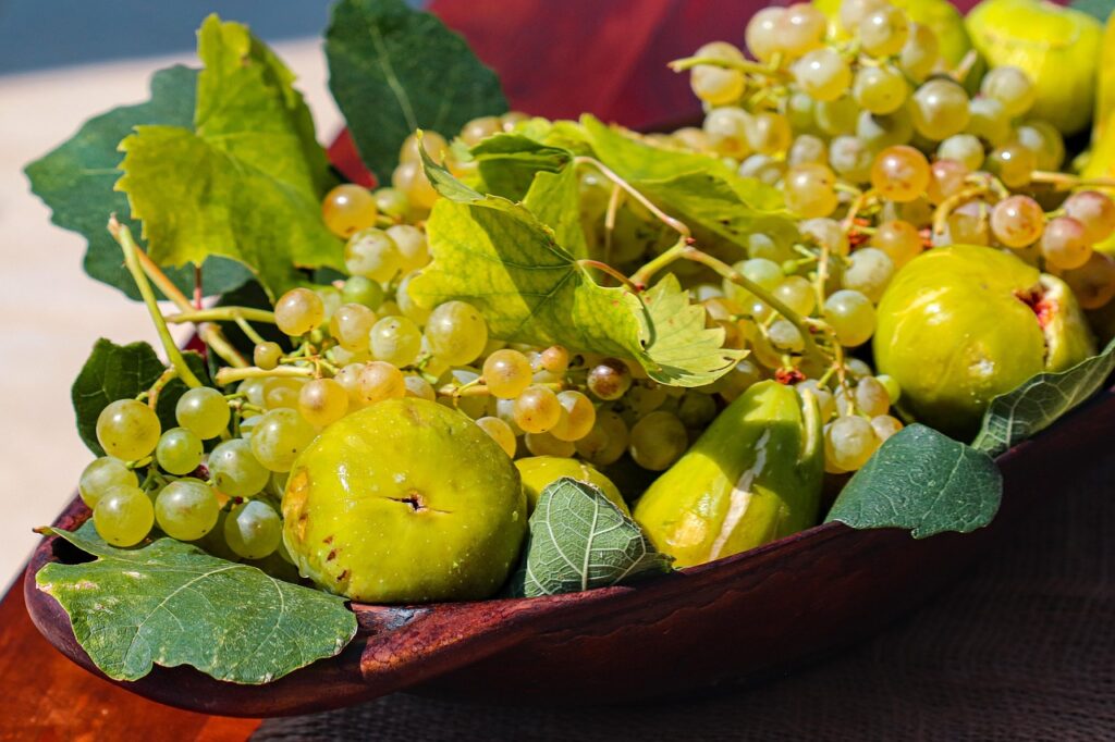 figs, grapes, vine leaves, fresh fruit, mediterranean food, organic produce, seasonal fruit, healthy eating, vineyard harvest, rustic bowl, fruit closeup, summer food, green grapes, nature's bounty, farm to table, natural lifestyle, sweet fruit, raw food, eco living, fruit composition, sunlit produce, rustic kitchen, botanical food, plant-based diet, country style